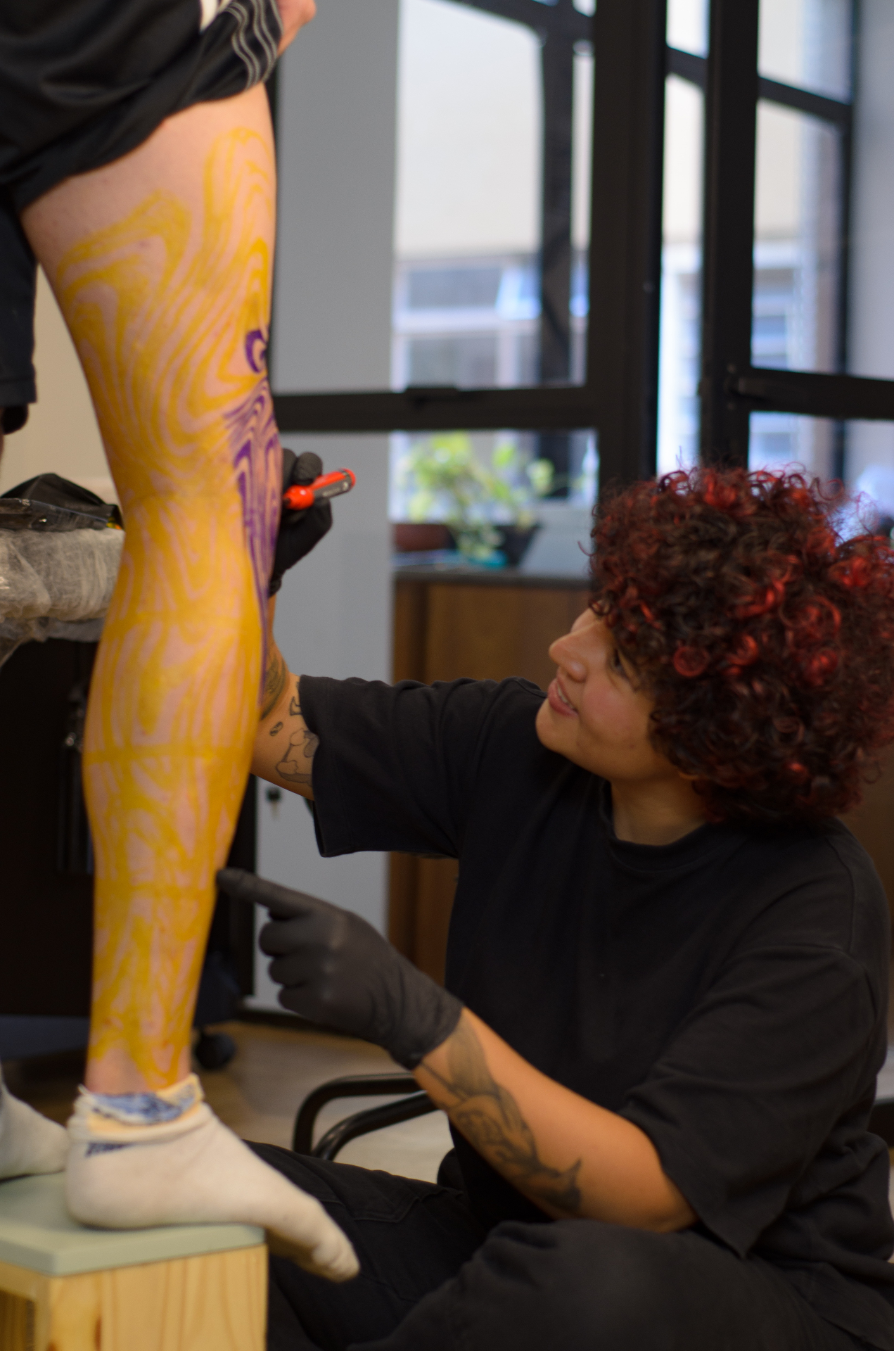 Piettra tatuando uma perna com padrão fluido em amarelo